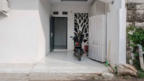 A motorcycle parked in a gated driveway, a white wall, and a door with a tree-like pattern. - KoolKost Syariah near Bintaro Jaya Xchange (South Tangerang)