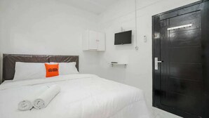 A hotel room with a bed, a TV mounted on the wall, a wardrobe, and a towel on the bed. - KoolKost Syariah near Bintaro Jaya Xchange (South Tangerang)