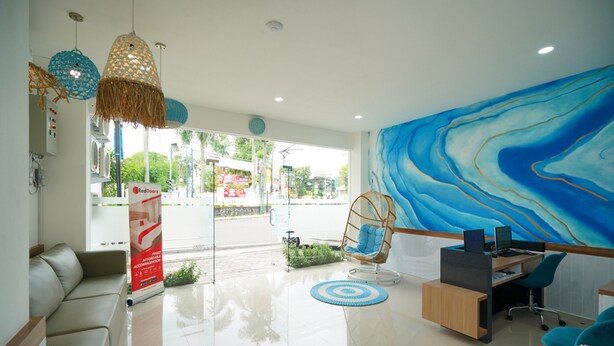 A modern reception area with a large blue abstract mural, a glass door entrance, a seating area with a sofa and chairs, and a desk with a computer.