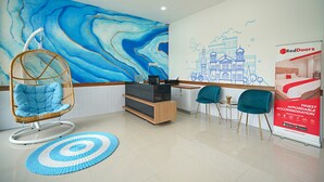 A reception area with a large blue mural, a wicker chair, a desk, and two teal chairs.