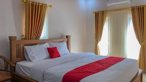 A neatly made bed with white linens and a red accent pillow, wooden headboard, and curtains. - RedDoorz near XT Square 3 (Yogyakarta)