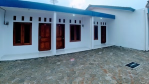A building with a white exterior and blue trim, featuring multiple wooden doors and windows. - RedDoorz near Exit Toll Jatiwarna 2 (Bekasi)