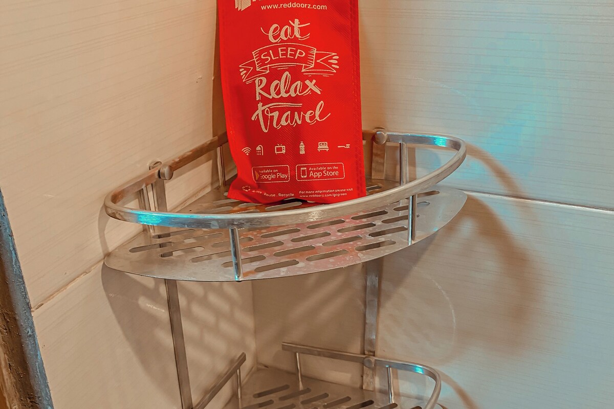 Un coin avec une étagère métallique adossée à un mur blanc, sur laquelle est posé un article promotionnel de la marque RedDoorz, de couleur rouge.