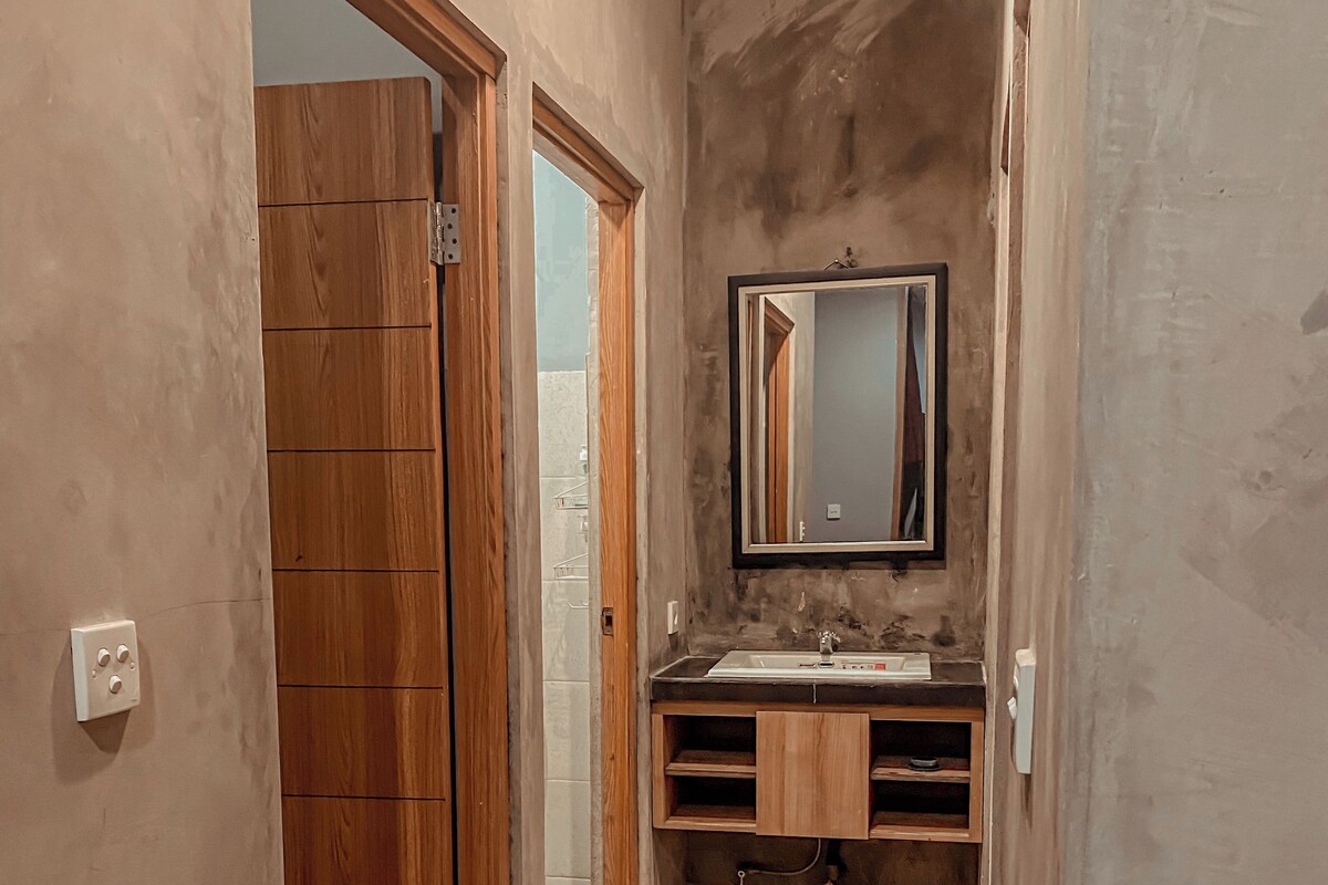 Een smalle gang met houten vloer die leidt naar een badkamer met een houten wastafel en een spiegel.