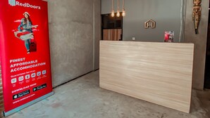 Ein Empfangsbereich mit einem hölzernen Empfangstresen, einer roten RedDoorz-Werbung und einer modernen Leuchte.