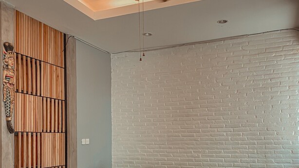 Ein Zimmer mit einer hölzernen Bank, einem Deckenventilator und einer weißen Ziegelwand.