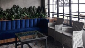 A modern lounge area with a blue sofa, wicker chairs, and a glass coffee table. - RedDoorz Plus @ Doorman Guest House (Bandung)