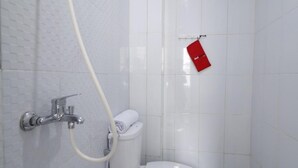 A bathroom with a white tiled wall, a toilet, a shower with a hose, and a red towel hanging on a hook. - RedDoorz Plus Syariah near Mall Pondok Indah (Jakarta)