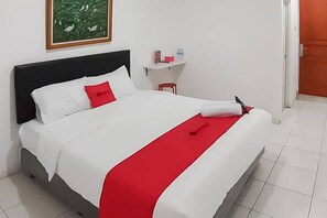 A neatly made bed with white and red bedding, a small red stool, and a framed picture on the wall. - RedDoorz Syariah @ Jl Raya Sukabumi (Pasirhalang)