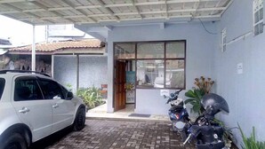 A building with a tiled roof, a parked car, and two motorcycles. - RedDoorz Syariah @ Hotel Kencana Tasikmalaya (Tasikmalaya)