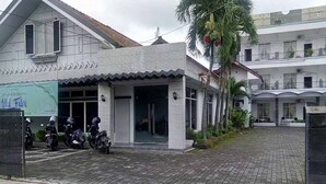 A building with a tiled entrance, a covered outdoor seating area, and a palm tree. - RedDoorz Syariah @ Hotel Kencana Tasikmalaya (Tasikmalaya)