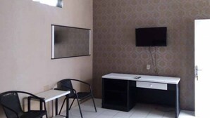 A small, private office with a desk and two chairs, a flat-screen TV mounted on the wall, and patterned wallpaper. - RedDoorz Syariah @ Hotel Kencana Tasikmalaya (Tasikmalaya)