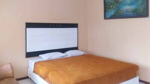 A bedroom with a bed, a headboard, a painting on the wall, and a chair. - RedDoorz Syariah @ Hotel Kencana Tasikmalaya (Tasikmalaya)