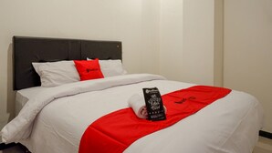 A neatly made bed with white and red bedding, a grey headboard, and a red towel with text on it. - RedDoorz @ Losari Area 2 (Makassar)