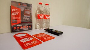 A table with a RedDoorz application poster, two V8 energy drink bottles, a remote control, and a 'Do Not Disturb' sign. - RedDoorz @ Losari Area 2 (Makassar)