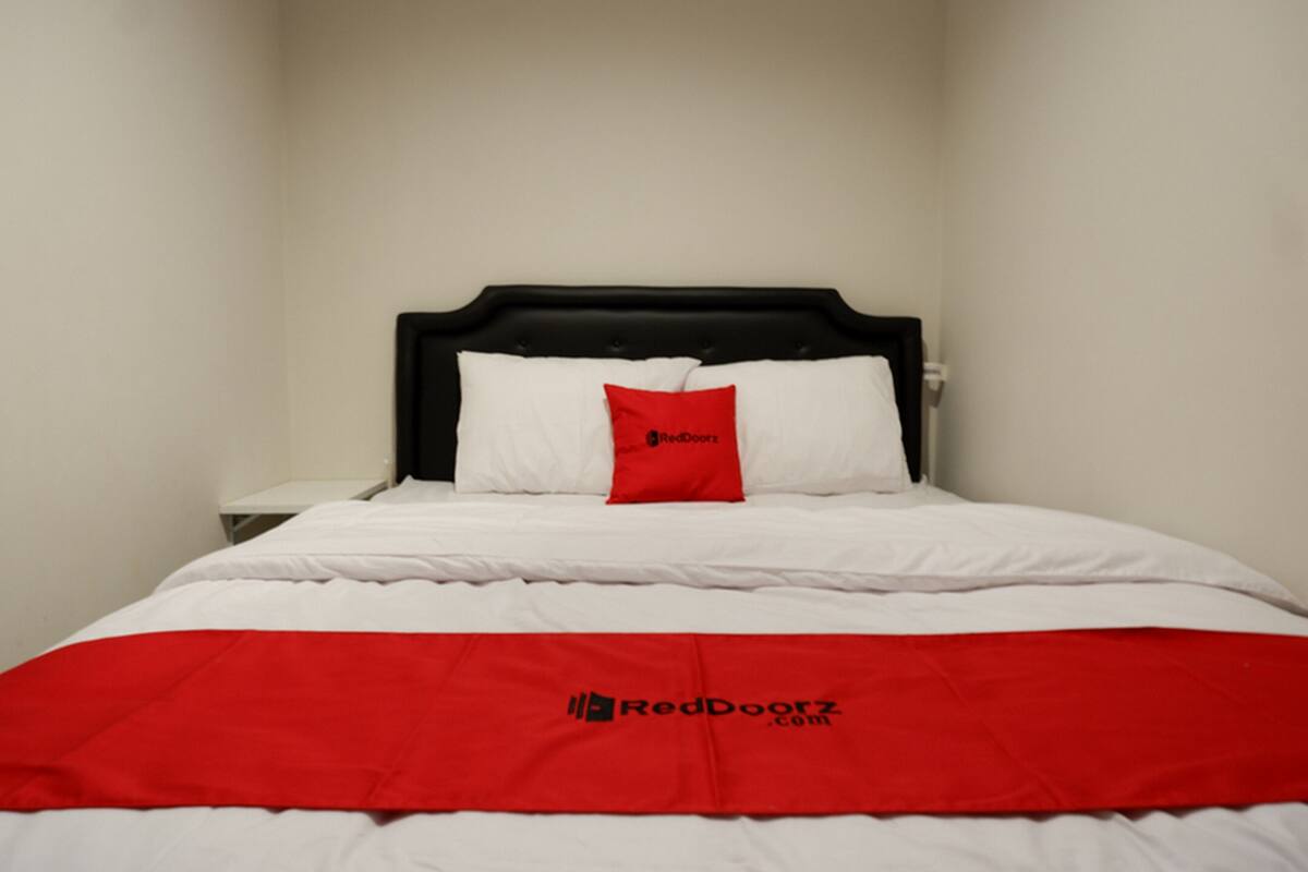 A bed with white bedding and a red blanket featuring a logo.