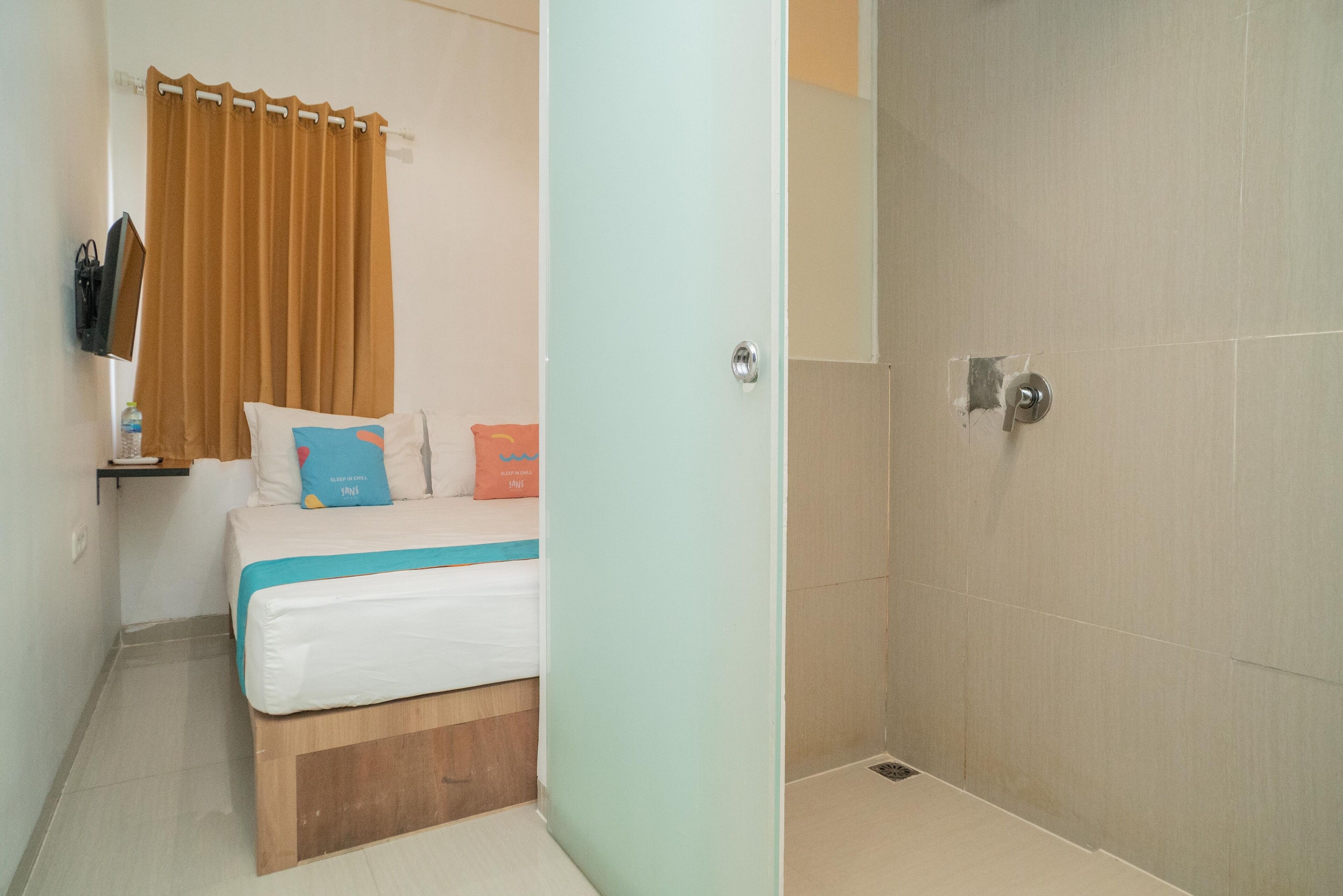 A bedroom with a bed, a nightstand, a TV, and a shower area.