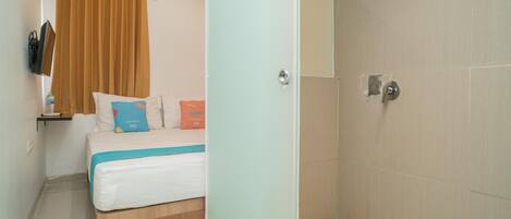 A bedroom with a bed, a nightstand, a TV, and a shower area.