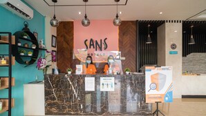 A hotel reception area with a marble counter, a sign for Sans Hotels, and a BoxHotel sign. - Sans Hotel Kupang Indah Surabaya (Surabaya)