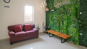 A room with a green wall, a sofa, a bench, a clock, and a 'No Smoking' sign. - Sans Hotel Kupang Indah Surabaya (Surabaya)