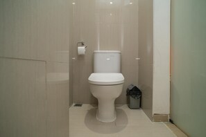 A modern bathroom with a white toilet, a trash bin, and a toilet paper holder on the wall.