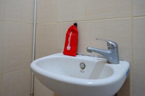 Un lavamanos blanco con grifo plateado y un bolso rojo colgado en la pared.