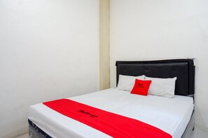 Una cama individual con cabecera negra, ropa de cama blanca y almohada decorativa roja.