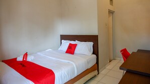 Een hotelkamer met een bed, een rood-witte spreideken, een houten hoofdbord, een klein tafeltje en een rode stoel.