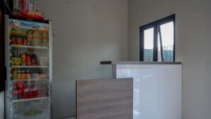 Een kamer met een Show Case koelkast gevuld met drankjes, een houten paneel en een raam met jaloezieën.
