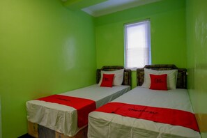 Une chambre avec deux lits simples, chacun recouvert d’une couverture rouge et agrémenté d’oreillers, et une fenêtre avec des stores.