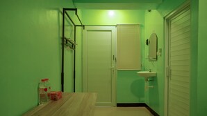 Ein kleiner Raum mit einem Holztisch, einer weißen Tür, einem Waschbecken und einem Fenster mit Jalousien.