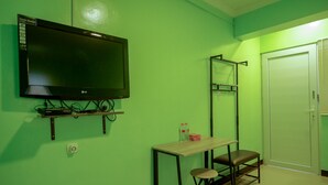 Ein Zimmer mit grüner Wand, einem an der Wand montierten Fernseher, einem kleinen Tisch und einem Stuhl sowie einer Tür.