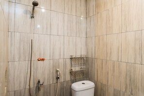 Et badeværelse med bruser, toilet og en lille hylde med toiletartikler.