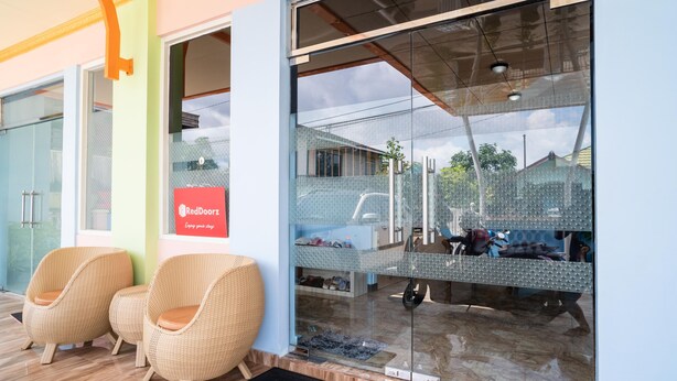 A reception area with wicker chairs, a RedDoorz sign, and a glass door reflecting the outside. - RedDoorz Syariah near Taman Siring 2 (Banjarmasin)