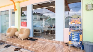 A reception area with two wicker chairs, a glass door entrance, and a signboard with COVID-19 guidelines. - RedDoorz Syariah near Taman Siring 2 (Banjarmasin)