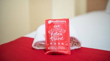 A neatly folded red towel with the RedDoorz logo and the words "sleep relax travel" on it, placed on a white bed.