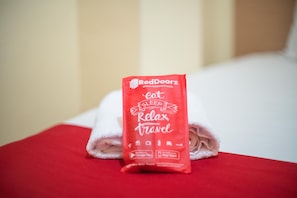 A neatly folded red towel with the RedDoorz logo and the words "sleep relax travel" on it, placed on a white bed. - RedDoorz Syariah near Taman Siring 2 (Banjarmasin)
