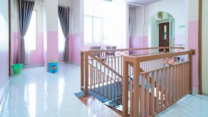 A spacious hallway with a wooden railing, a staircase, and a large window allowing natural light. - RedDoorz Syariah near Taman Siring 2 (Banjarmasin)