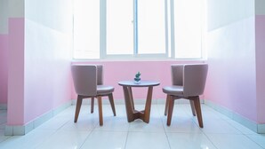 A room with two chairs and a small table, a window with blinds, and pink walls. - RedDoorz Syariah near Taman Siring 2 (Banjarmasin)