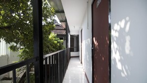 A narrow corridor with a tiled floor, a black metal railing, and a white wall with a red door. - RedDoorz near Riau Junction Mall 2 (Bandung)