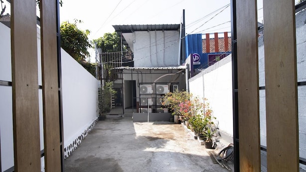 A narrow alleyway with a white building, a blue banner, and potted plants. - RedDoorz near Riau Junction Mall 2 (Bandung)