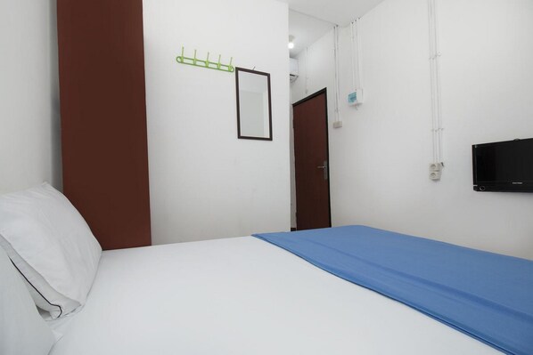A hotel room with a bed, a TV mounted on the wall, and a coat rack with hangers.