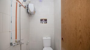 A small bathroom with a toilet, a shower with a hose, and a sign on the wall. - RedDoorz near Riau Junction Mall 2 (Bandung)
