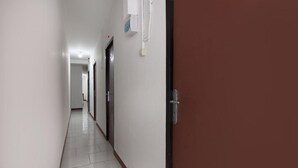 A long, narrow hallway with white walls and a brown door on the right. - RedDoorz near Riau Junction Mall 2 (Bandung)