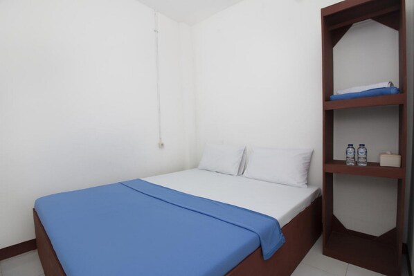 A simple, clean room with a bed, a shelf with water bottles, and a white wall. - RedDoorz near Riau Junction Mall 2 (Bandung)