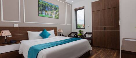 A hotel room with a large bed, a painting of a waterfall, wooden furniture, and a window with a view.