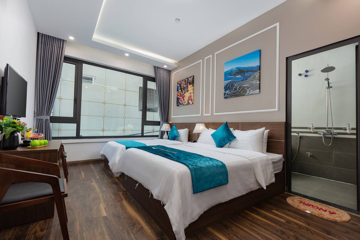 A modern hotel room with a large bed, a desk with a chair, a TV, and a shower area.