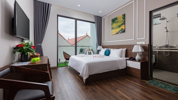 Una habitación de hotel moderna con una cama grande, un escritorio con televisor de pantalla plana, zona de ducha y vistas a edificios.