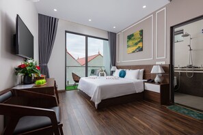 Ein modernes Hotelzimmer mit einem großen Bett, einem Schreibtisch mit Flachbildfernseher, einer Dusche und Blick auf umliegende Gebäude.