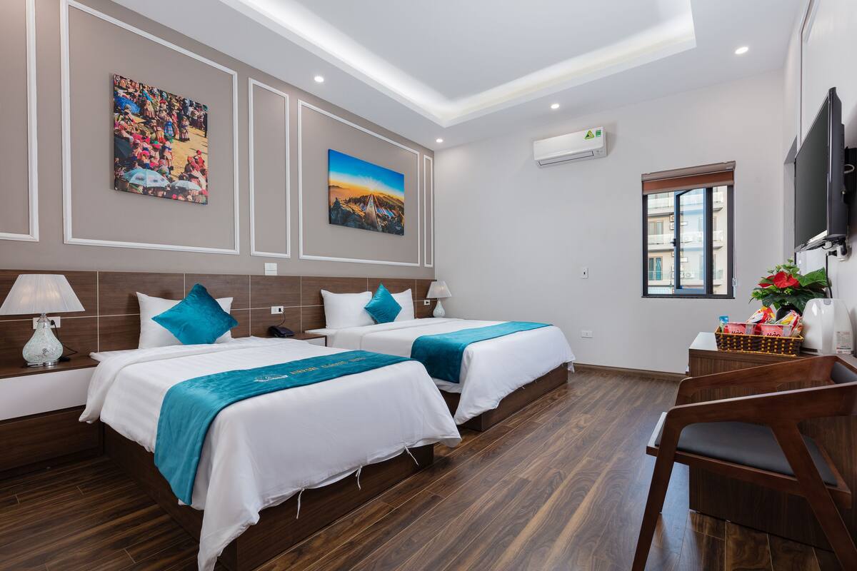A hotel room with two beds, a desk, a chair, a TV, and artwork on the walls.